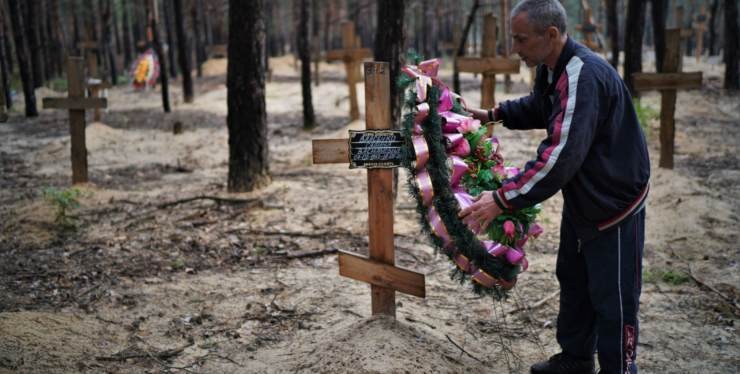 Ucraina, un uomo mette una corona di fiori su una delle tombe riesumate