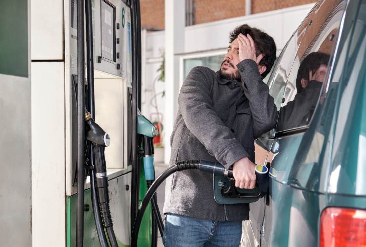 Giovane che fa rifornimento al suo veicolo mentre guarda preoccupato per gli alti prezzi del gas